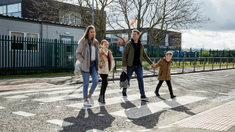 Image shows a family using a zebra crossing outside a school