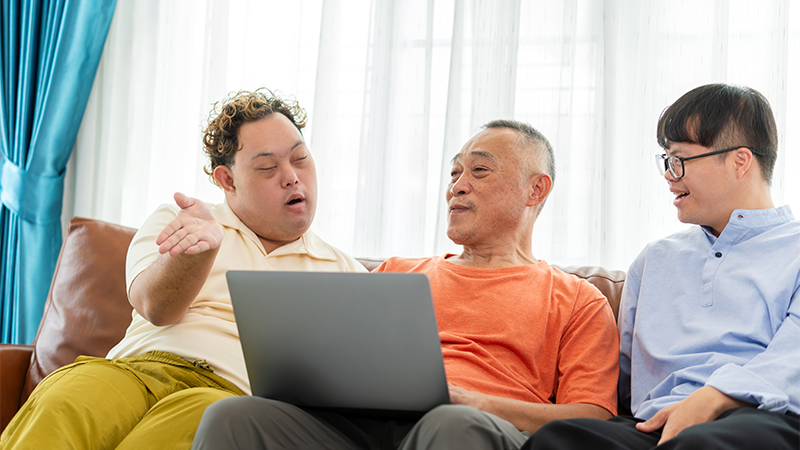 Three people sitting together on a couch, smiling and looking at a laptop screen