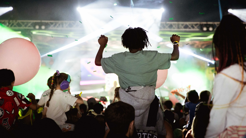 A child sitting on shoulders in a crowd at a concert