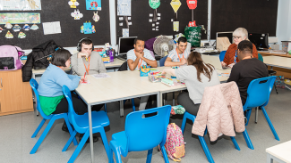 A group of people sitting around a table in a classroom, engaging in various activities with art supplies and papers